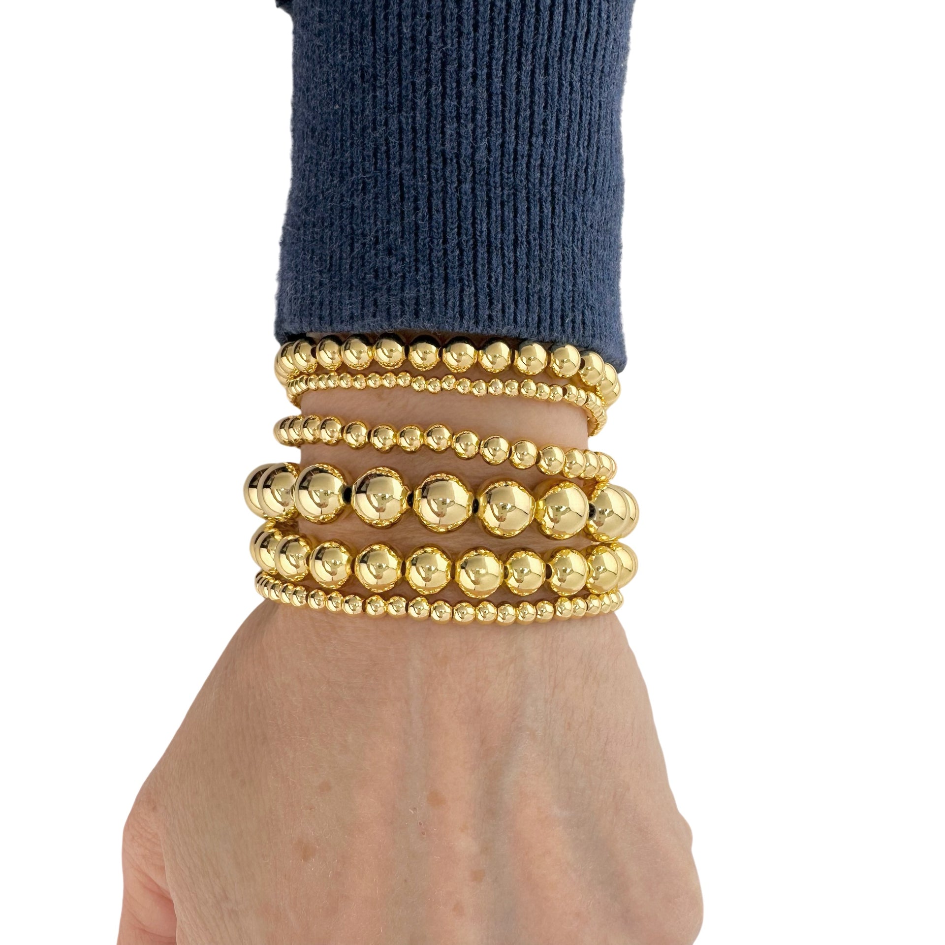 Gold beaded bracelets on a wrist with a white background