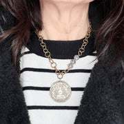 Person wearing a gold chain necklace with a large silver pendant on a black and white striped sweater.