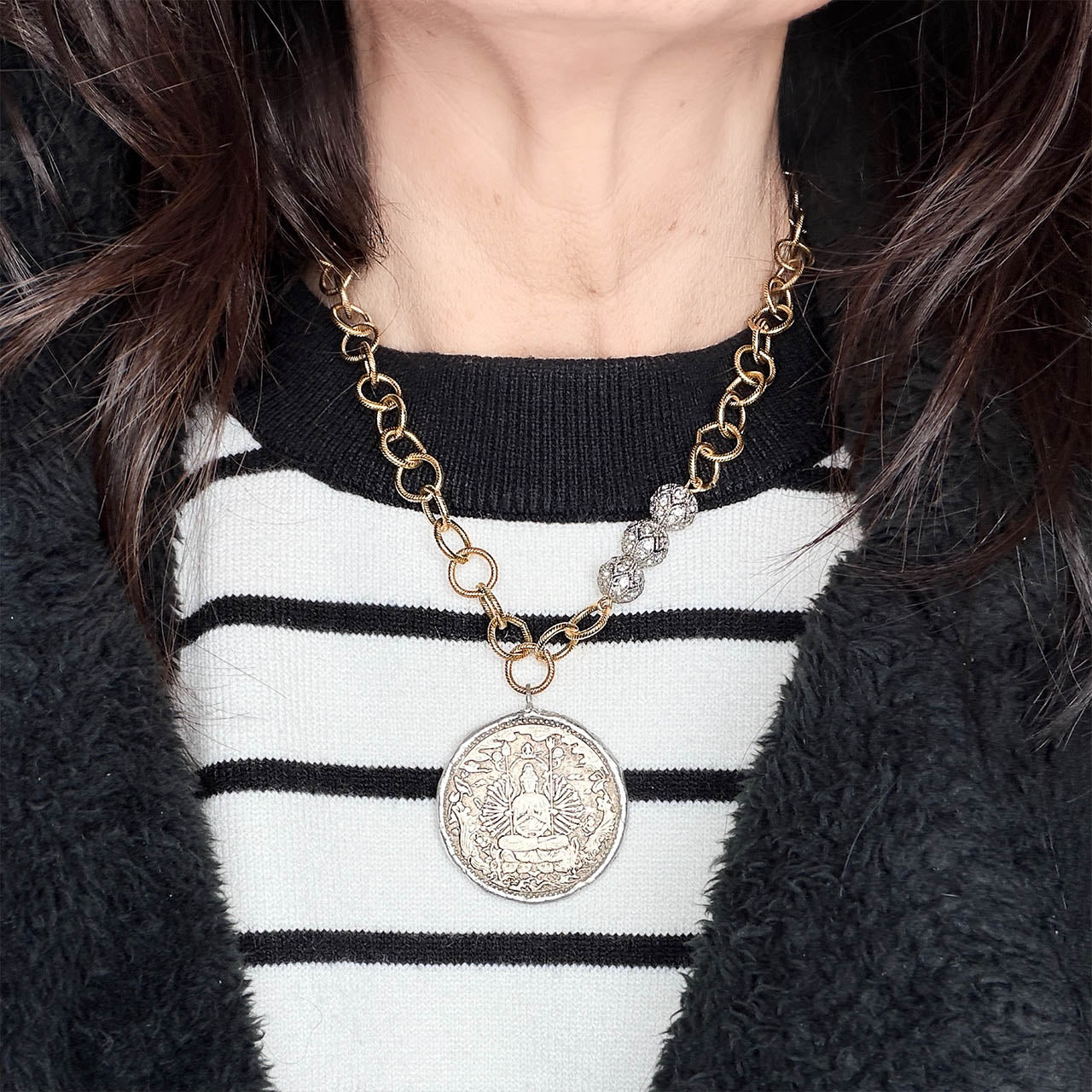 Person wearing a gold chain necklace with a large silver pendant on a black and white striped sweater.