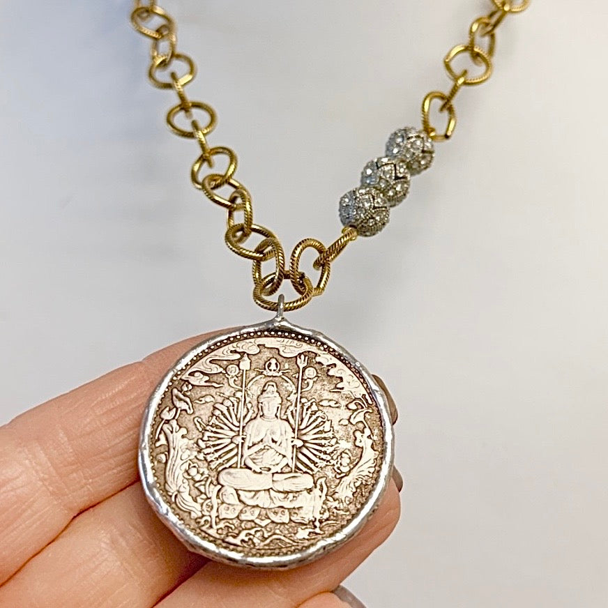 Gold chain necklace with a detailed coin pendant held by a hand against a light background