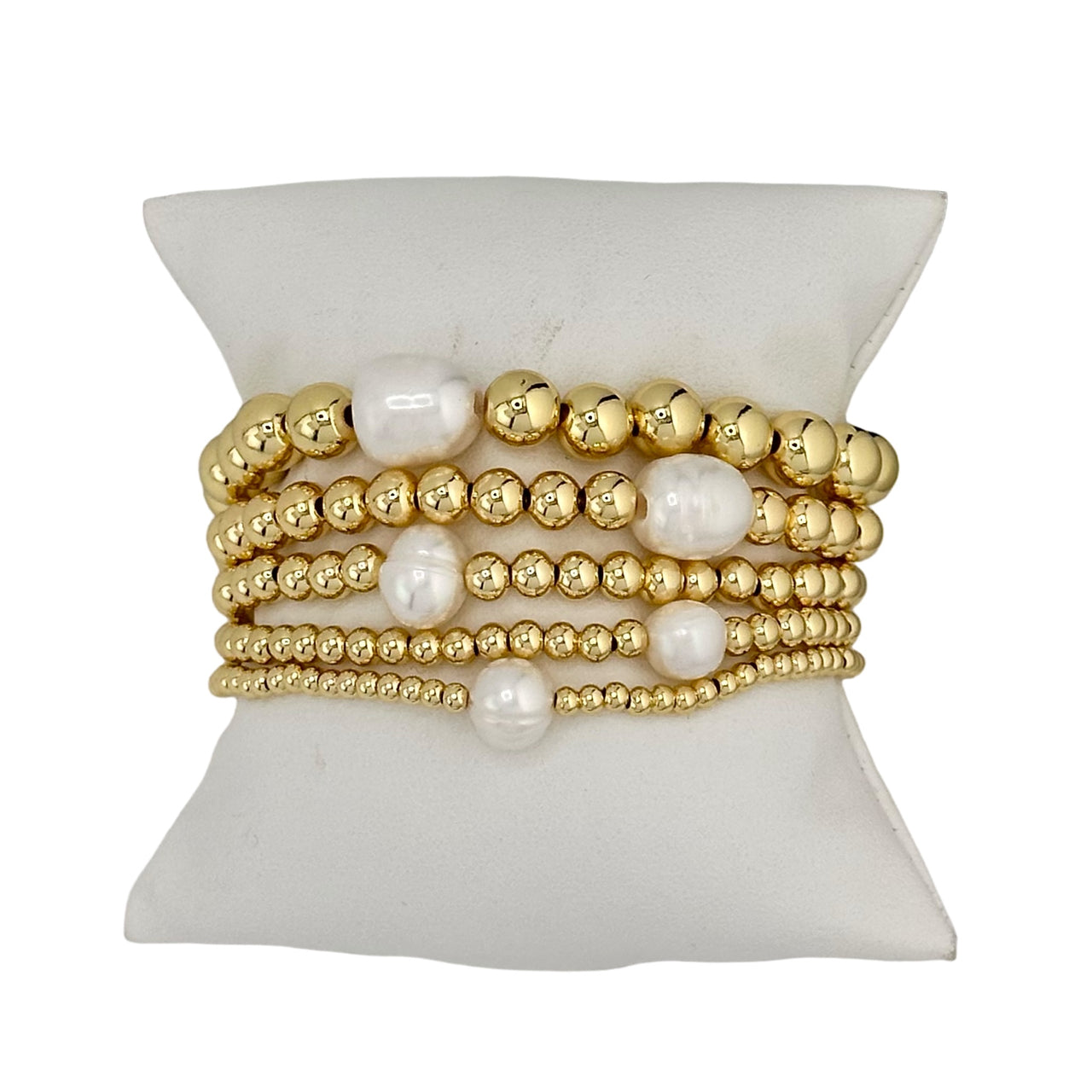 A stack of gold-colored beaded bracelets with white pearls, displayed on a flat surface.