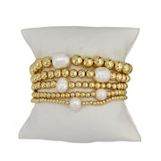 A stack of gold-colored beaded bracelets with white pearls, displayed on a flat surface.
