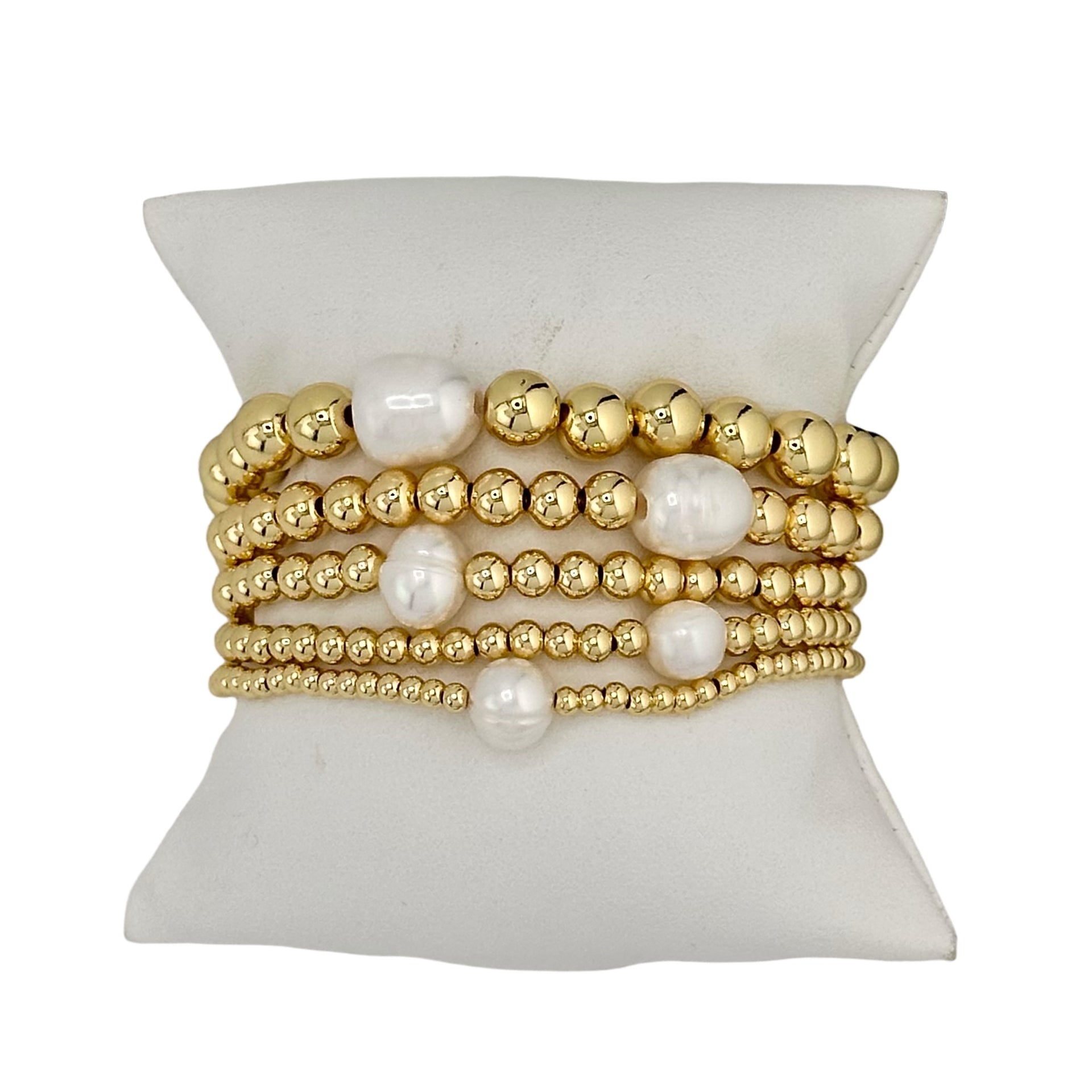 A stack of gold-colored beaded bracelets with white pearls, displayed on a flat surface.
