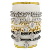 A collection of beaded bracelets with various metallic finishes and Saint medals displayed on a cylindrical stand.