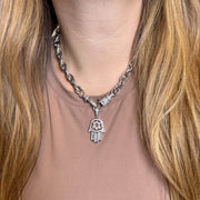 Necklace with a Hamsa hand pendant worn by a person with long blonde hair.