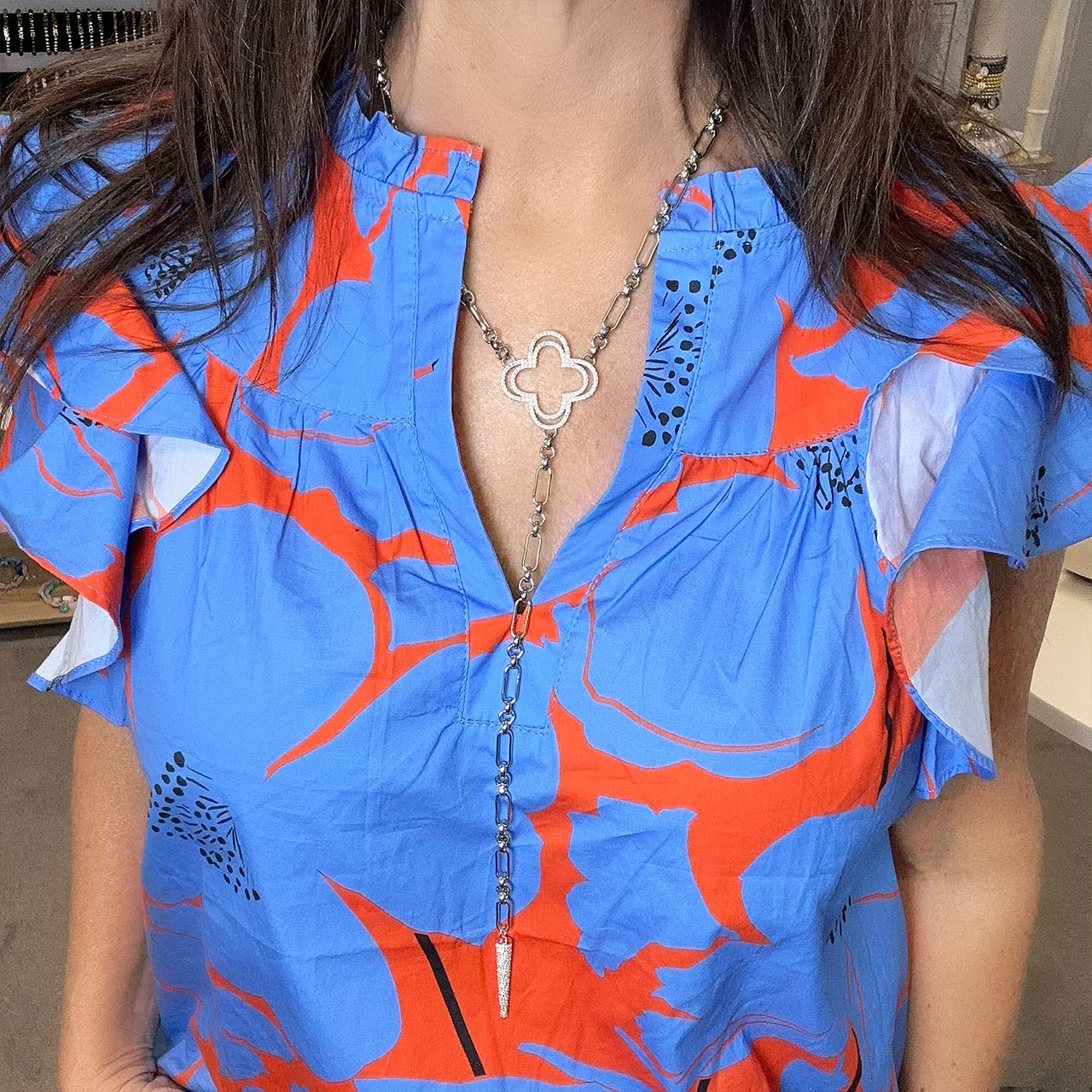 Person wearing a blue and orange floral dress with a deep neckline and a long necklace.