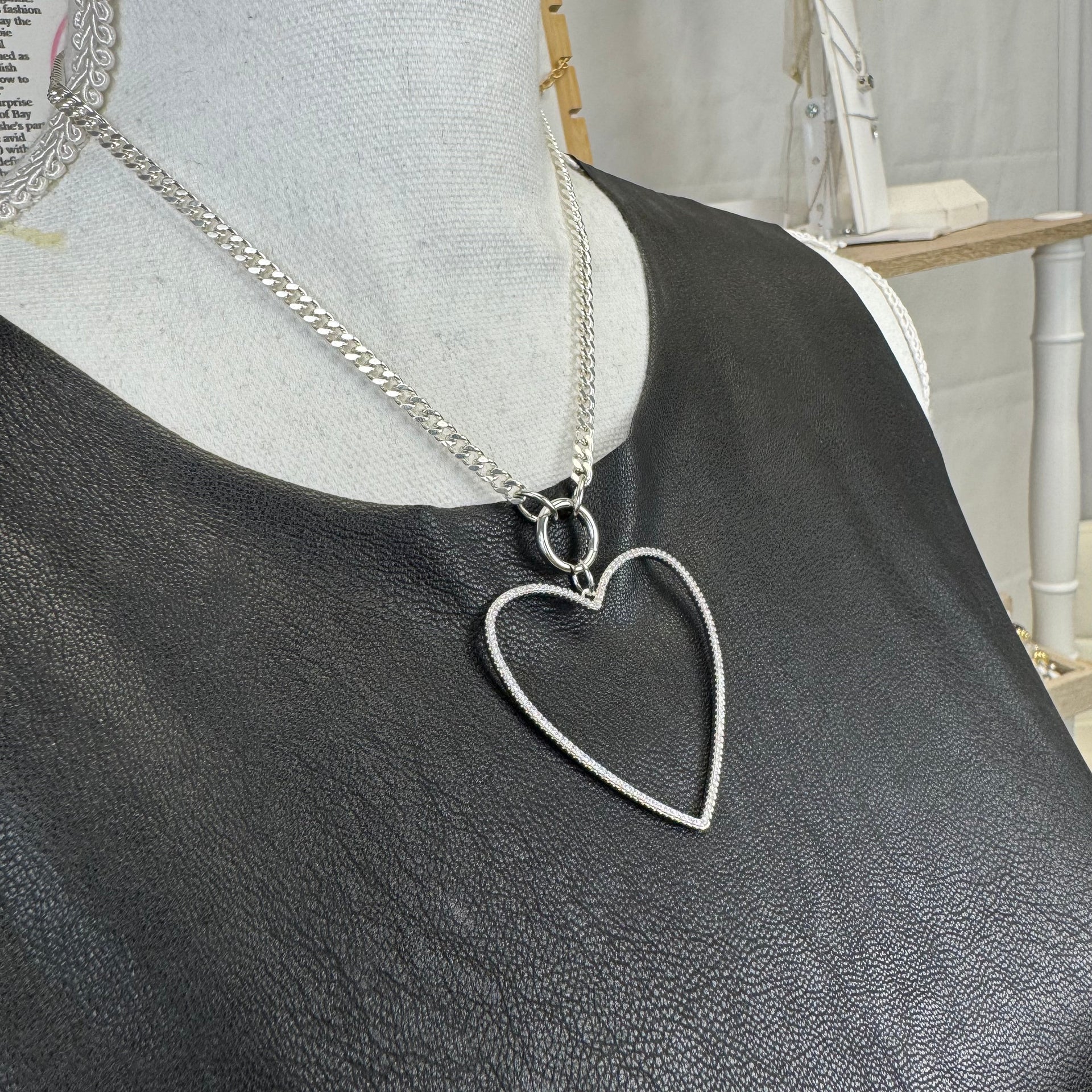 Delicate silver heart pendant with open frame design on display