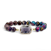 Bellissima Emerald Cut Crystal Gemstone Bracelet in Purple with dark gemstone beads, gold-tone accents, and lavender crystal centerpiece