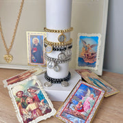 catholic medal saint beaded bracelets gold and silver stack displayed with candle by love lisa