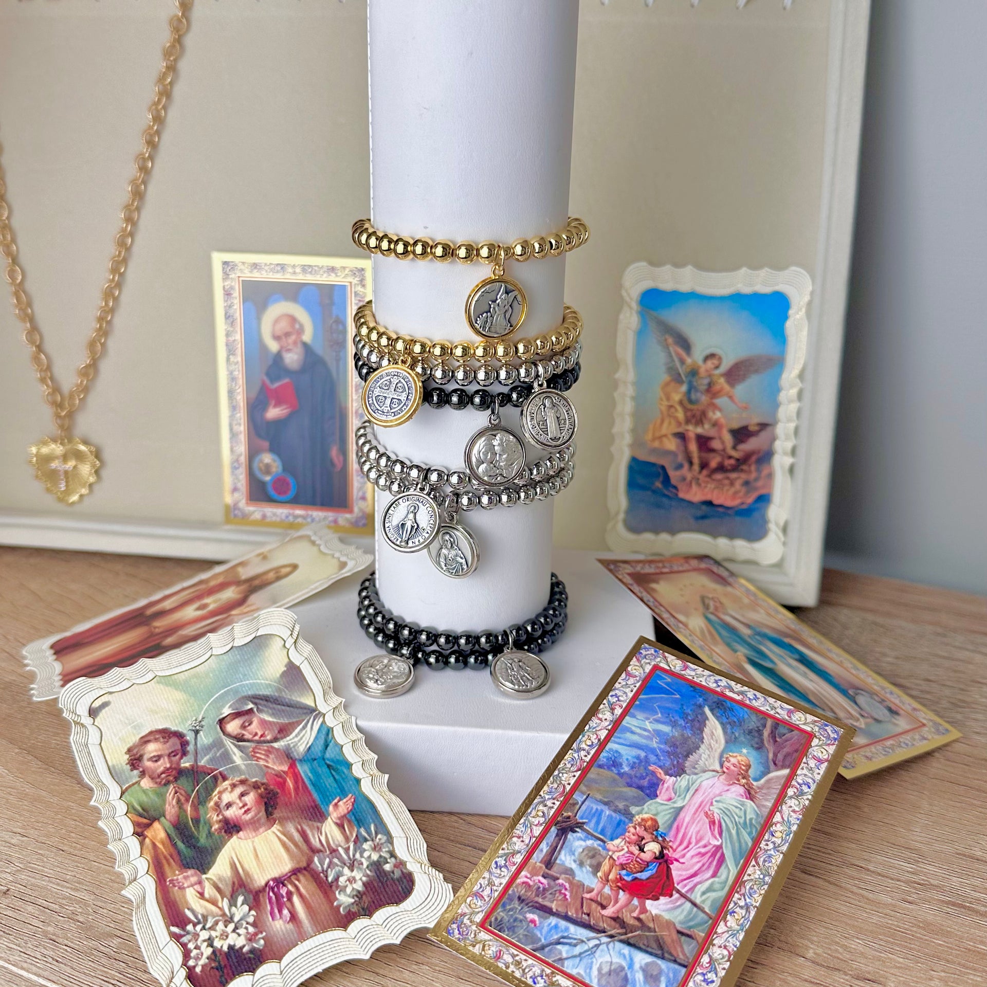 catholic medal saint beaded bracelets gold and silver stack displayed with candle by love lisa