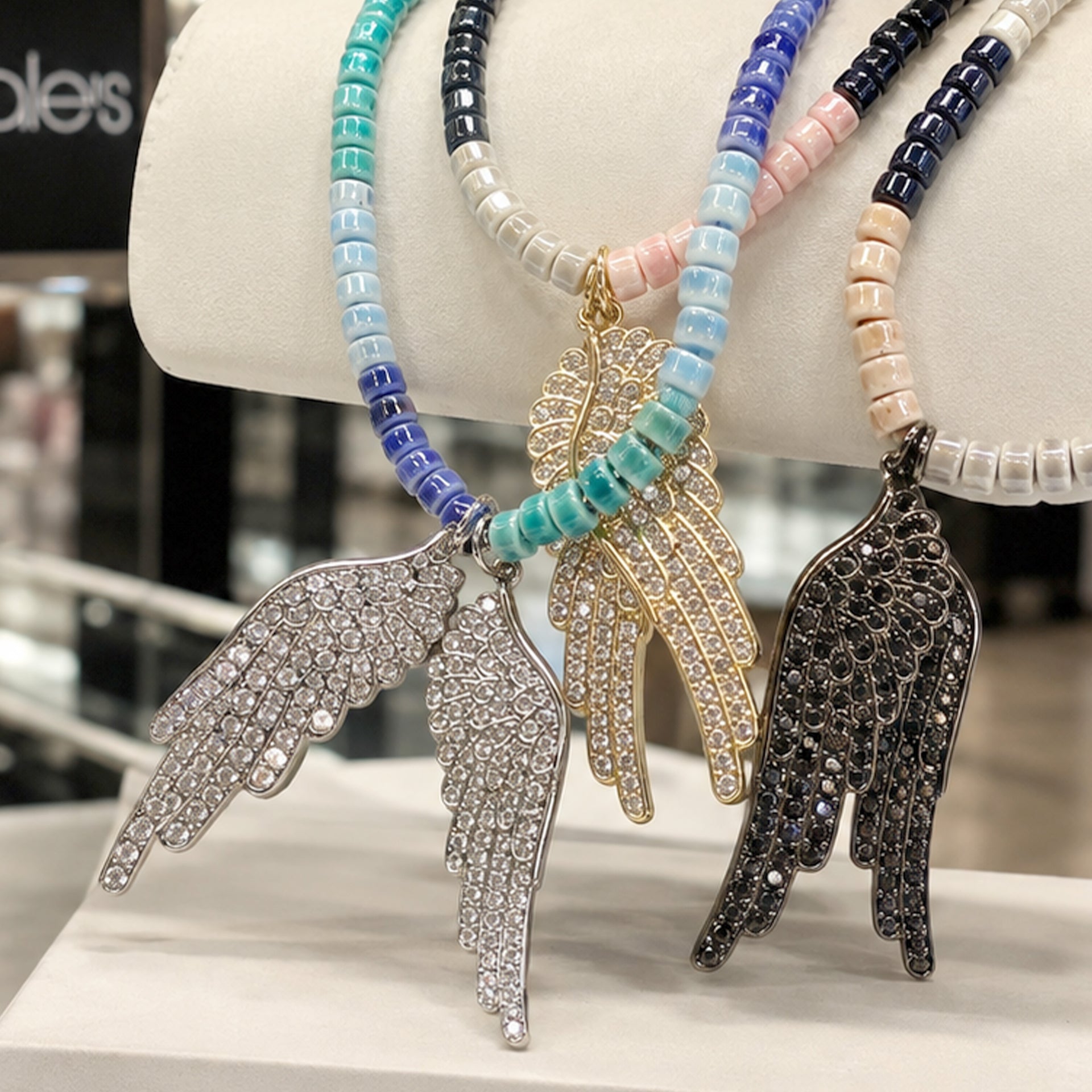ove Lisa Celeste Angel Wing Ceramic Beaded Necklace shown in a boutique display with ceramic beads and oversized crystal angel wing pendant