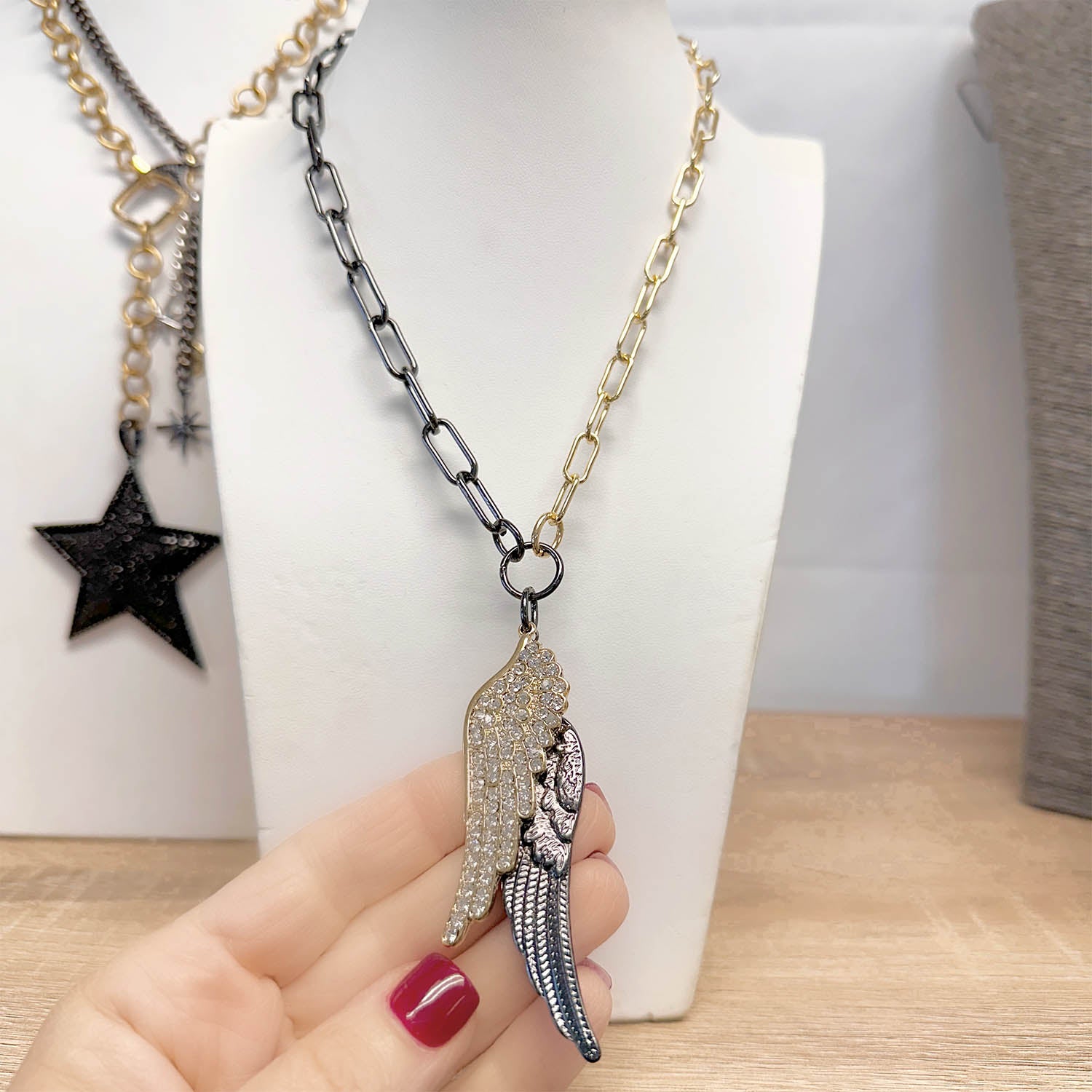 Necklace with a wing-shaped pendant held by a hand against a neutral background