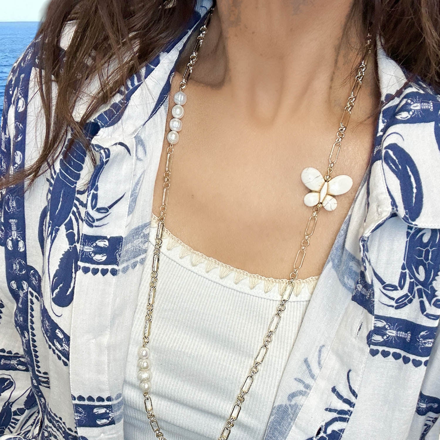 Person wearing a butterfly necklace with a blue and white patterned garment.