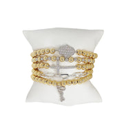 stack of hailey beaded love bracelets with hamsa,cross and love charm in gold and silver on jewelry pillow