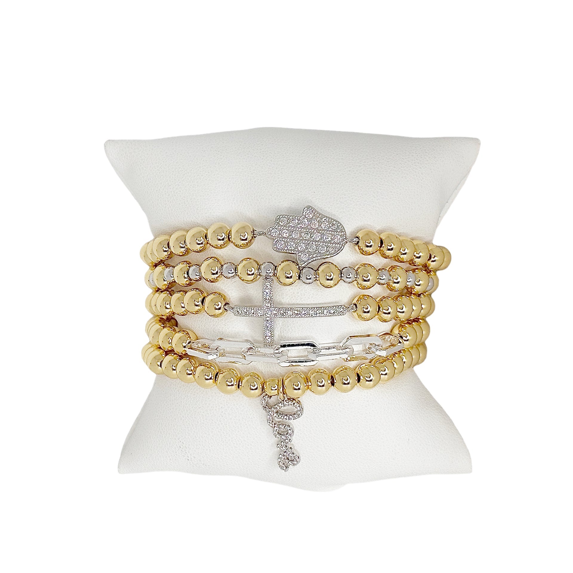 stack of hailey beaded love bracelets with hamsa,cross and love charm in gold and silver on jewelry pillow