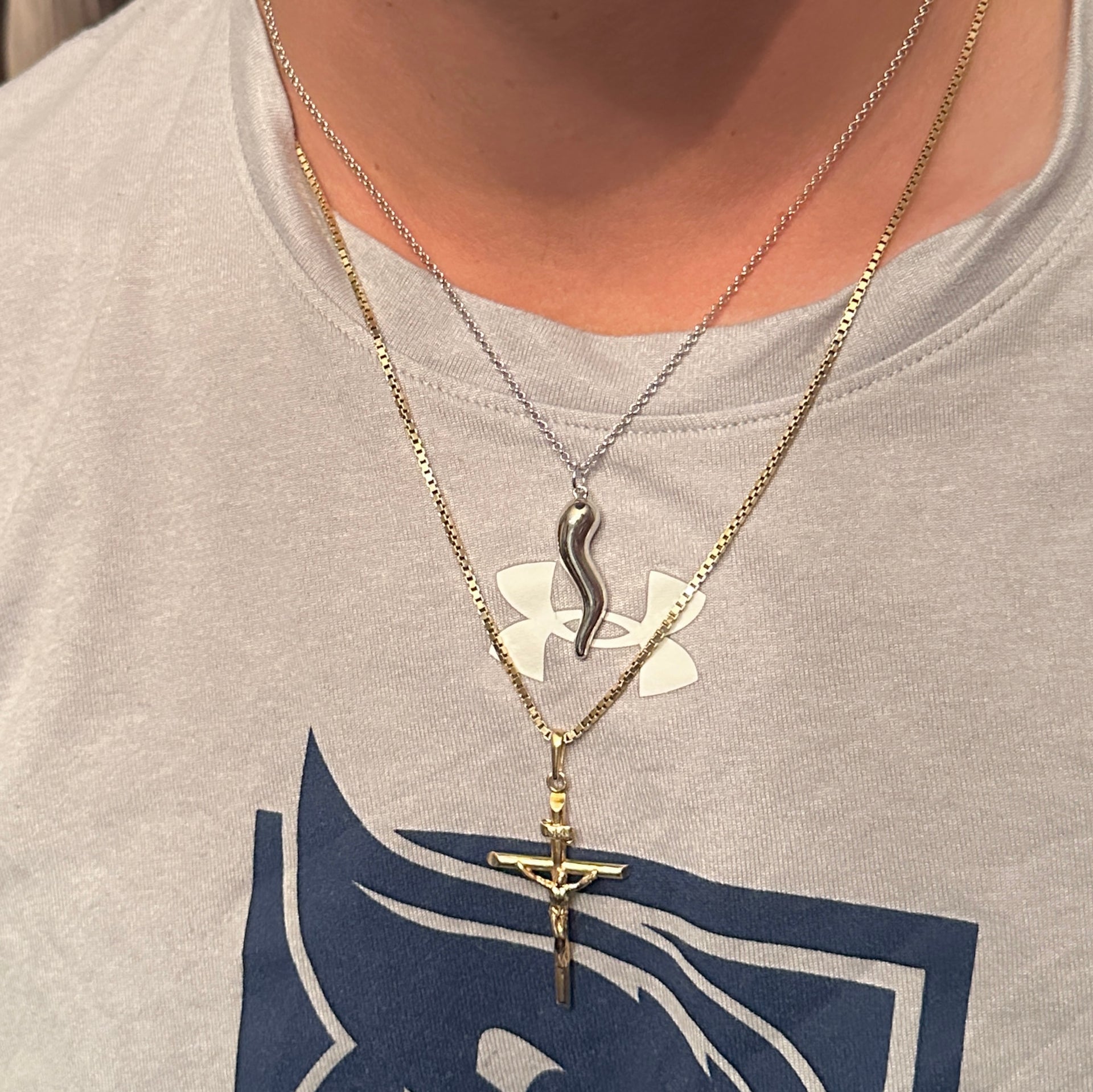 Two necklaces with pendants on a person wearing a gray shirt with a logo.