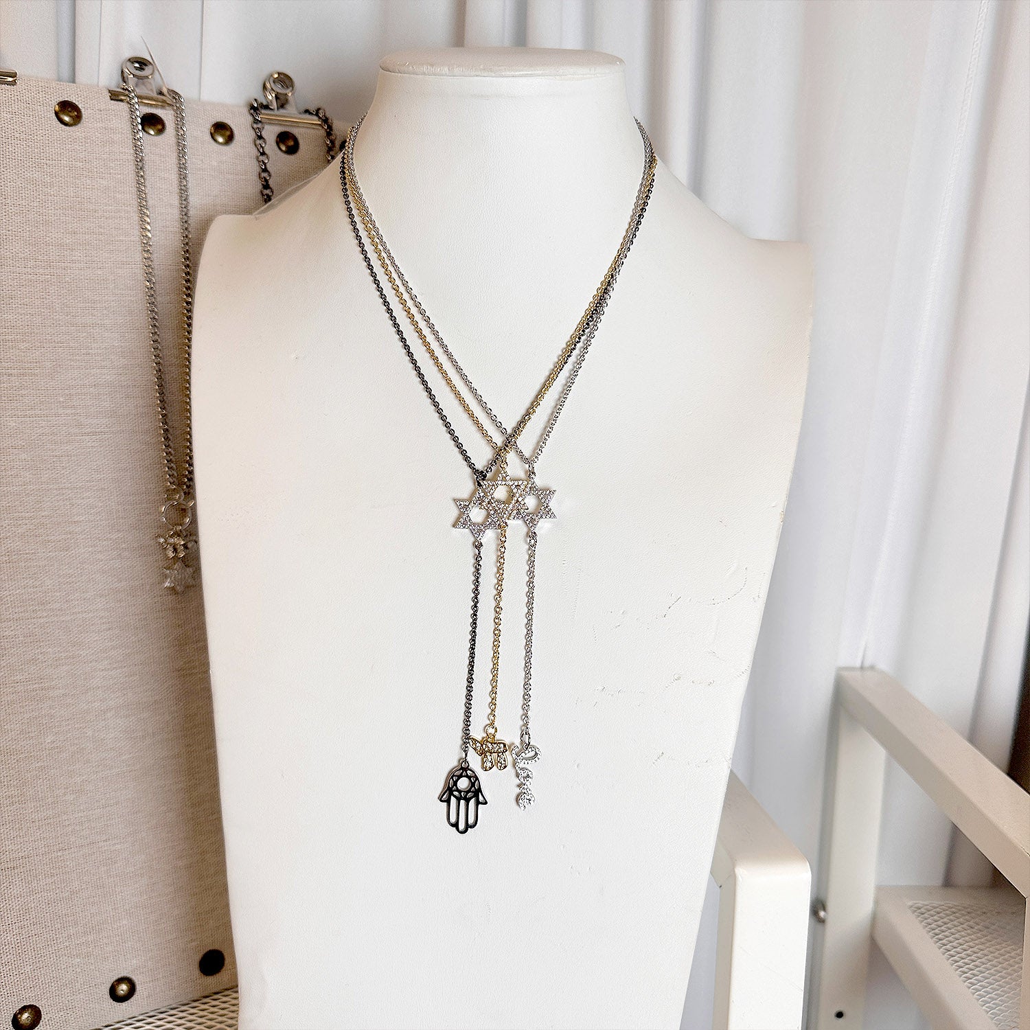 Necklace with star and hand of faith charms on a mannequin bust against a white curtain background.