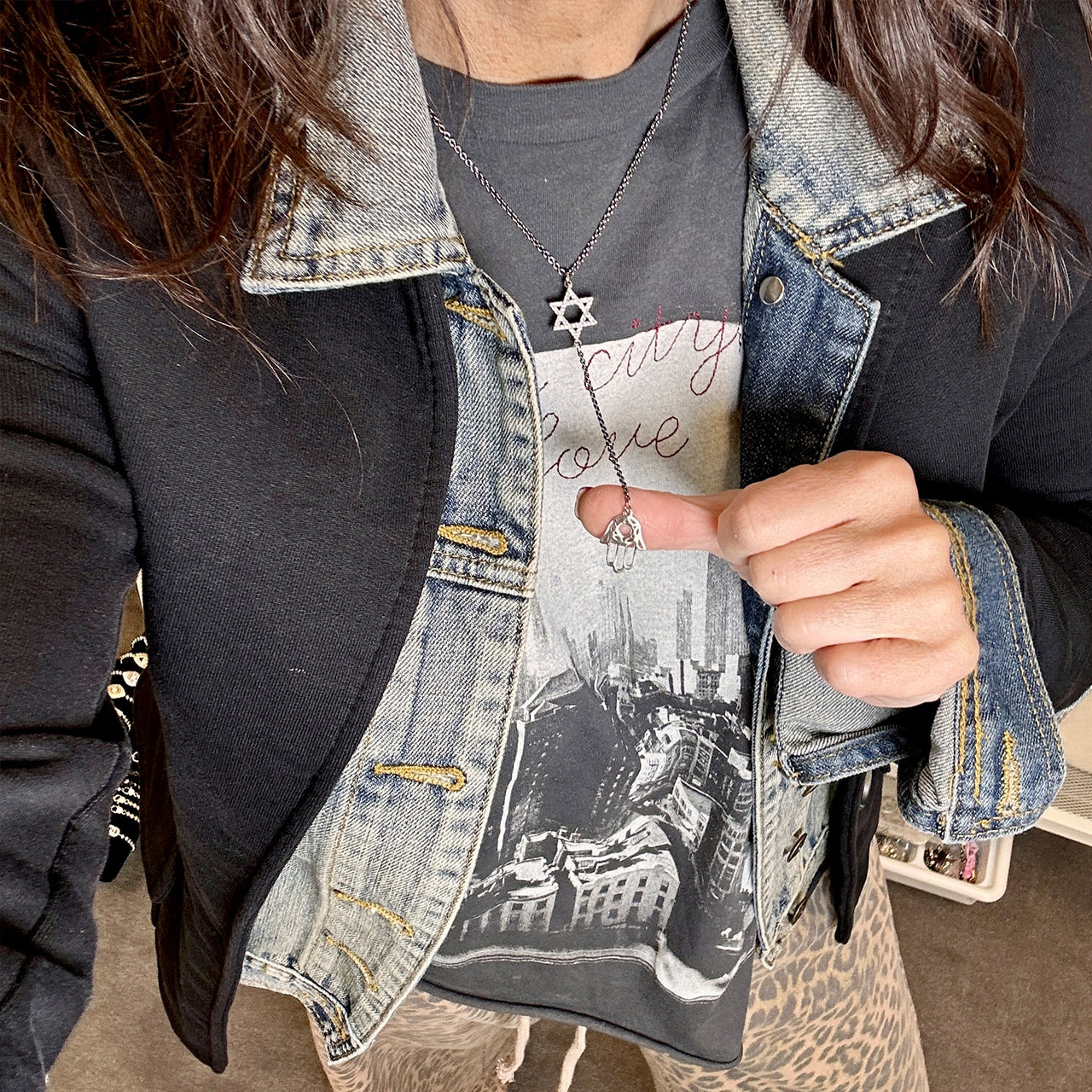 Person wearing a denim jacket over a graphic t-shirt with a cityscape design.