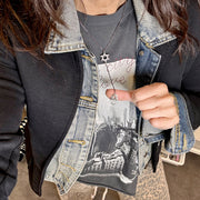 Person wearing a denim jacket over a graphic t-shirt with a cityscape design.