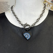 Gunmetal-tone heart pendant with evil eye motif in vibrant blue and white on display