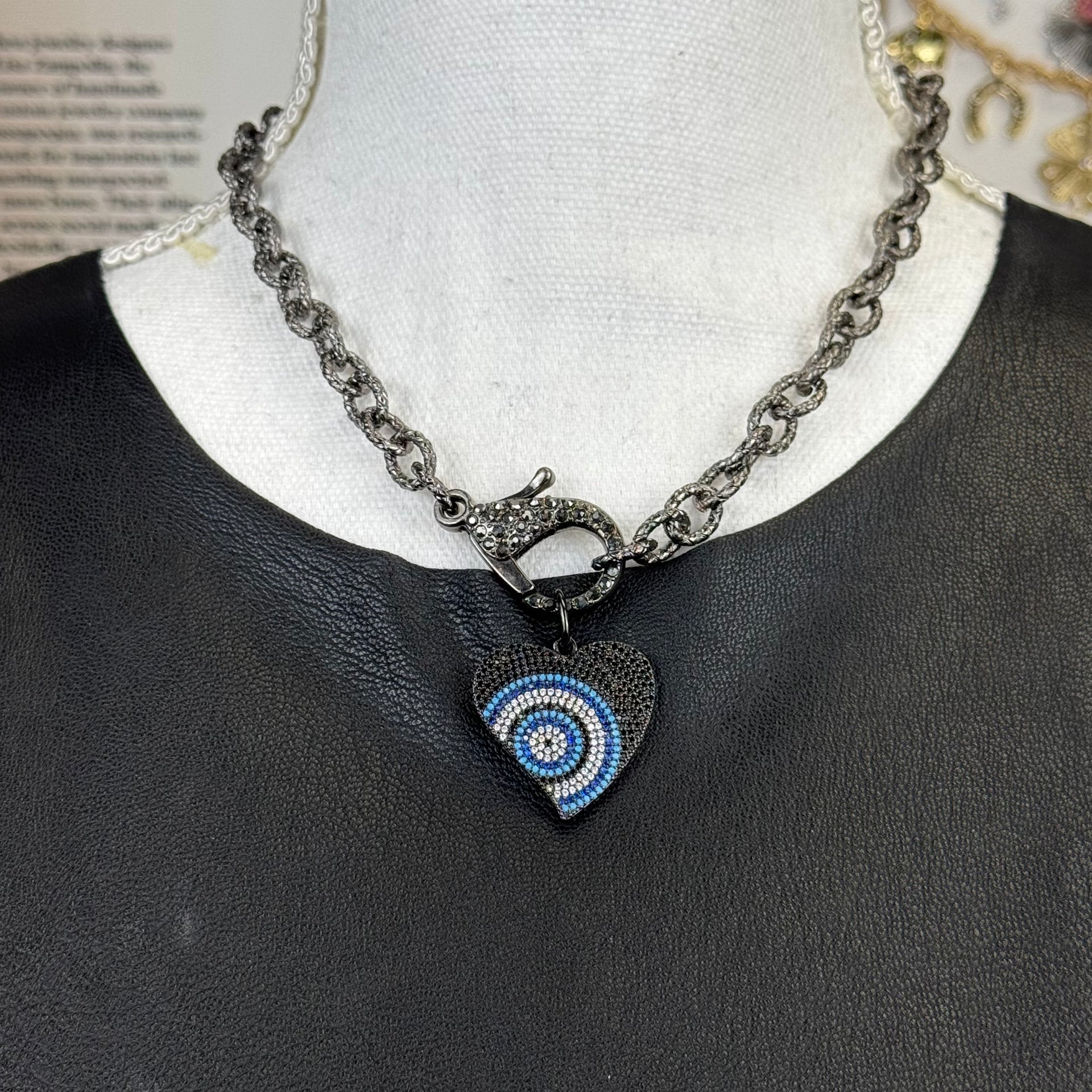 Gunmetal-tone heart pendant with evil eye motif in vibrant blue and white on display