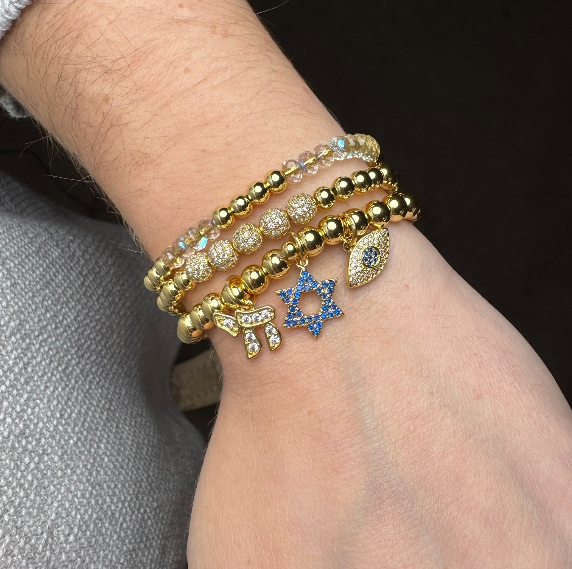 love lisa gold faith and protection charm bracelet worn stacked with blue pave star of david chai charm and evil eye