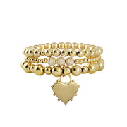 A gold bracelet stack featuring a series of round beads and a heart-shaped charm.