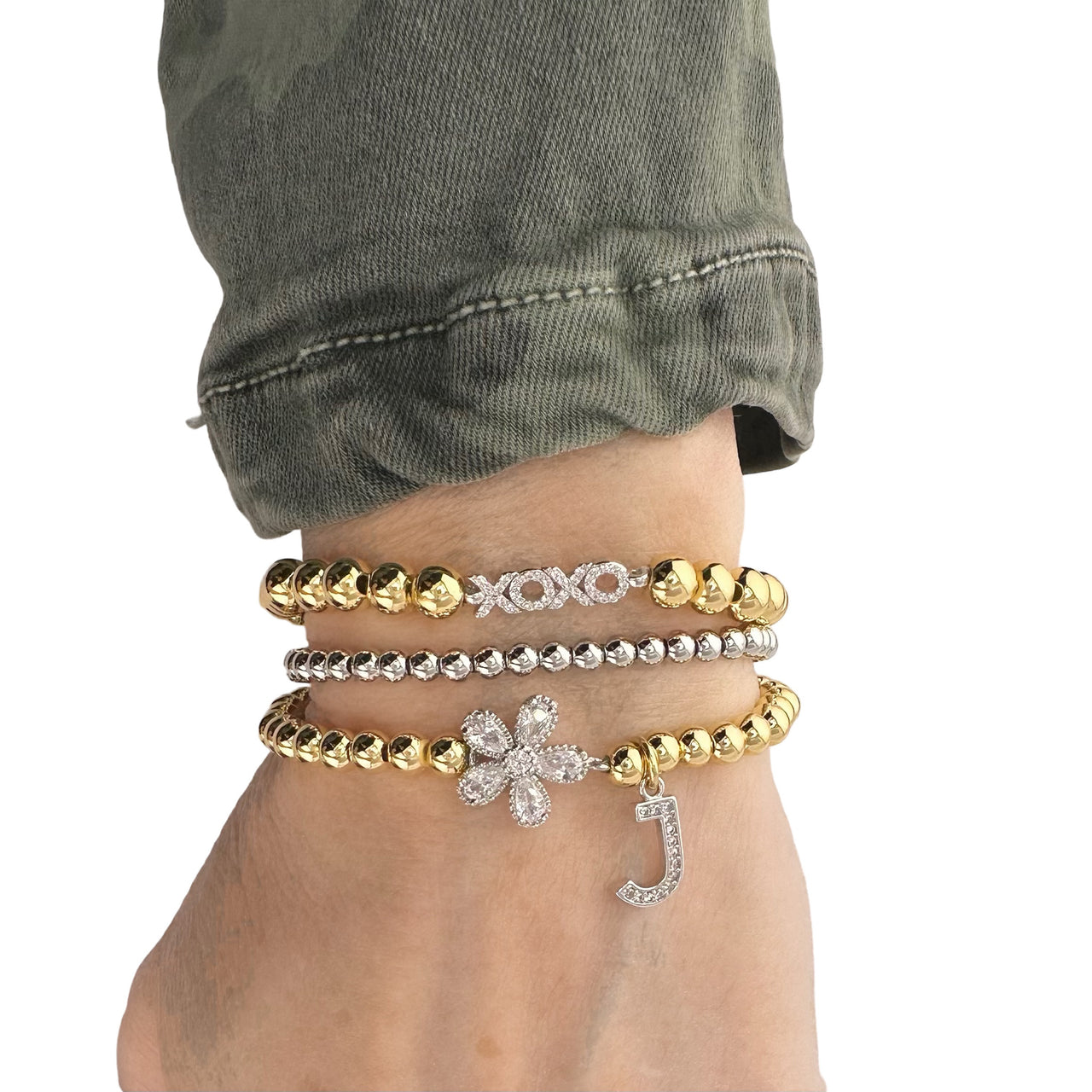 love lisa flower initial charm bracelet worn on wrist stacked with gold and silver beaded bracelets featuring crystal flower charm and pave initial charm