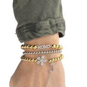 love lisa flower initial charm bracelet worn on wrist stacked with gold and silver beaded bracelets featuring crystal flower charm and pave initial charm