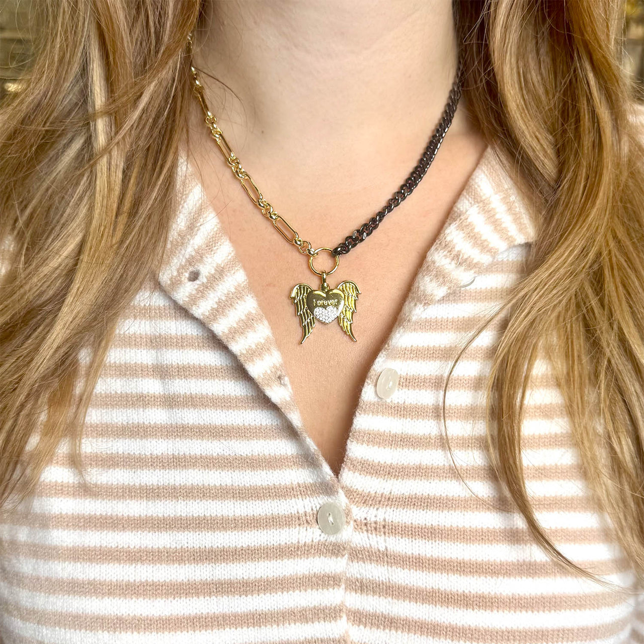 Close-up of a person wearing a gold necklace with an angel pendant on a striped shirt.