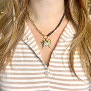 Close-up of a person wearing a gold necklace with an angel pendant on a striped shirt.