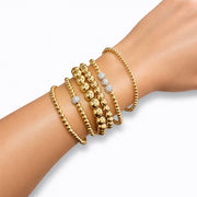 A series of six gold beaded bracelets stacked together, featuring a variety of round beads.