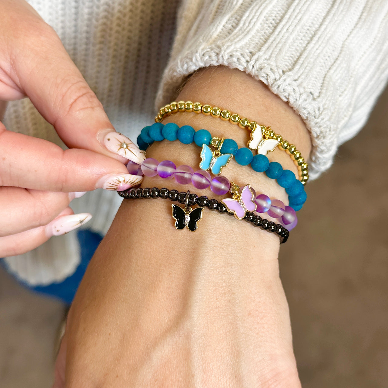 Close-up of a wrist wearing multiple colorful beaded bracelets with butterfly charms.