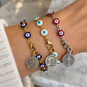 Love Lisa Hannah Evil Eye Saint Medal Bracelets worn together on the wrist in red, turquoise, blue, and black colorways with gold-tone and silver-tone links and assorted religious saint medals