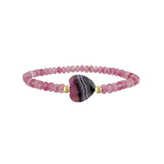 Bracelet with pink beads and a central purple and black heart-shaped worry stone on a white background
