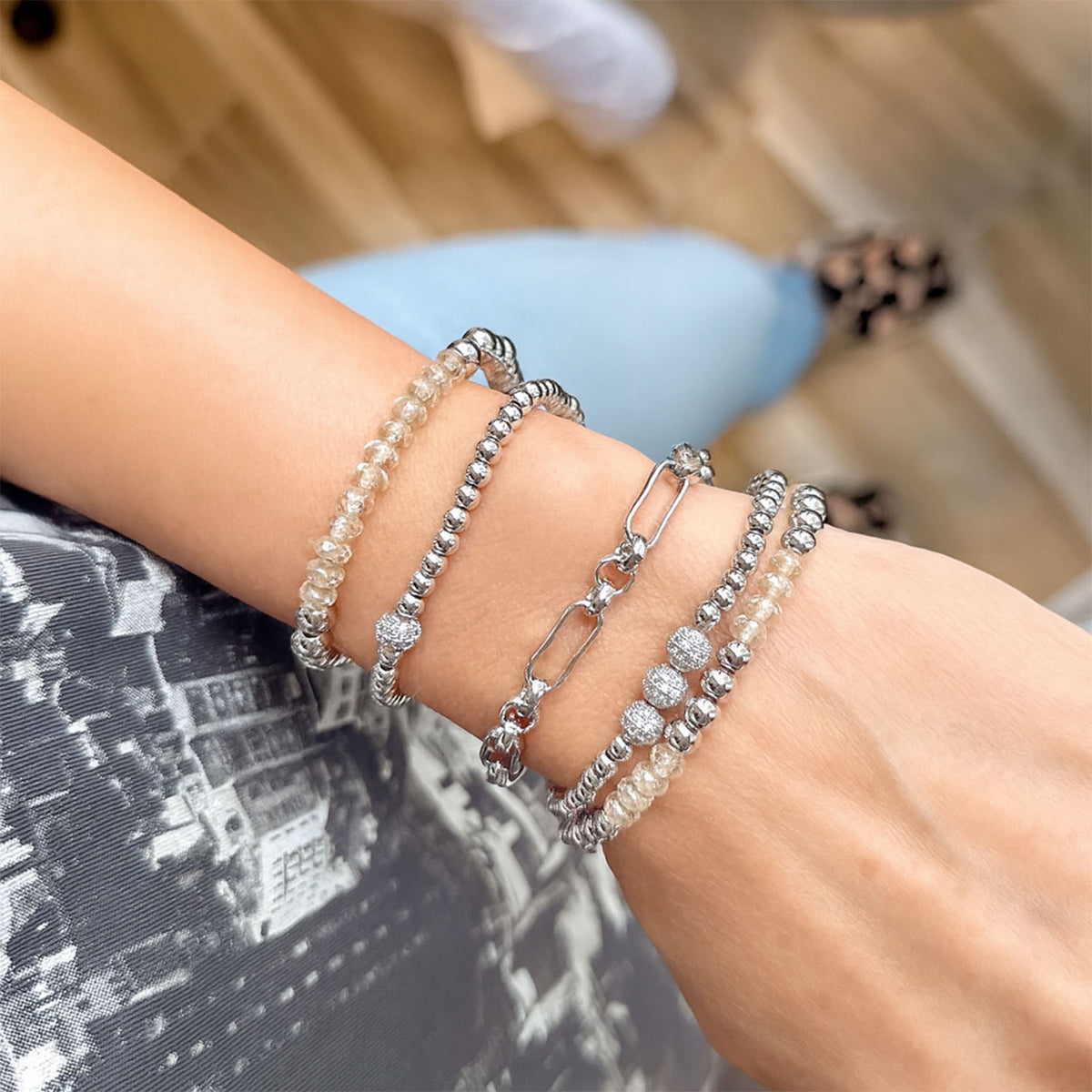 Close-up of a wrist wearing multiple silver bracelets with beads and chain links.