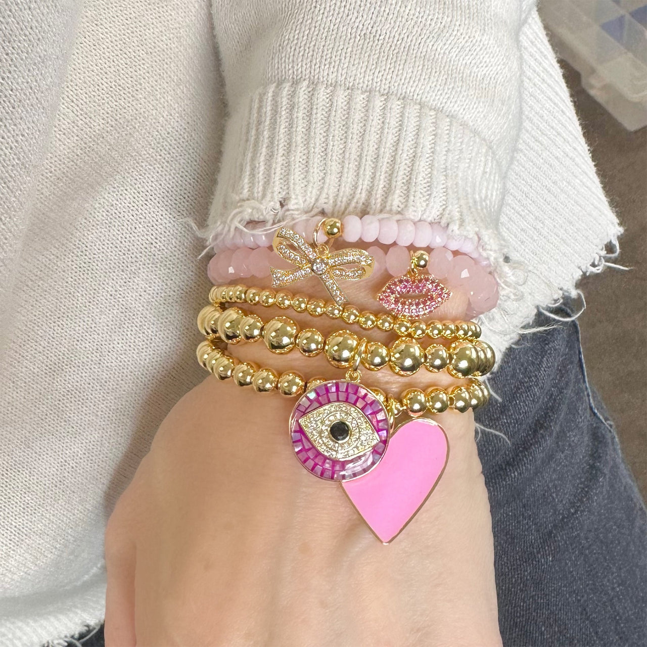 pink harper pretty cz bow bracelet with faceted beads and sparkling gold cz bow charm by Love Lisa stacked on wrist with other charm bracelets. 