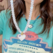 Person wearing a necklace with a heart-shaped pendant on a turquoise shirt.