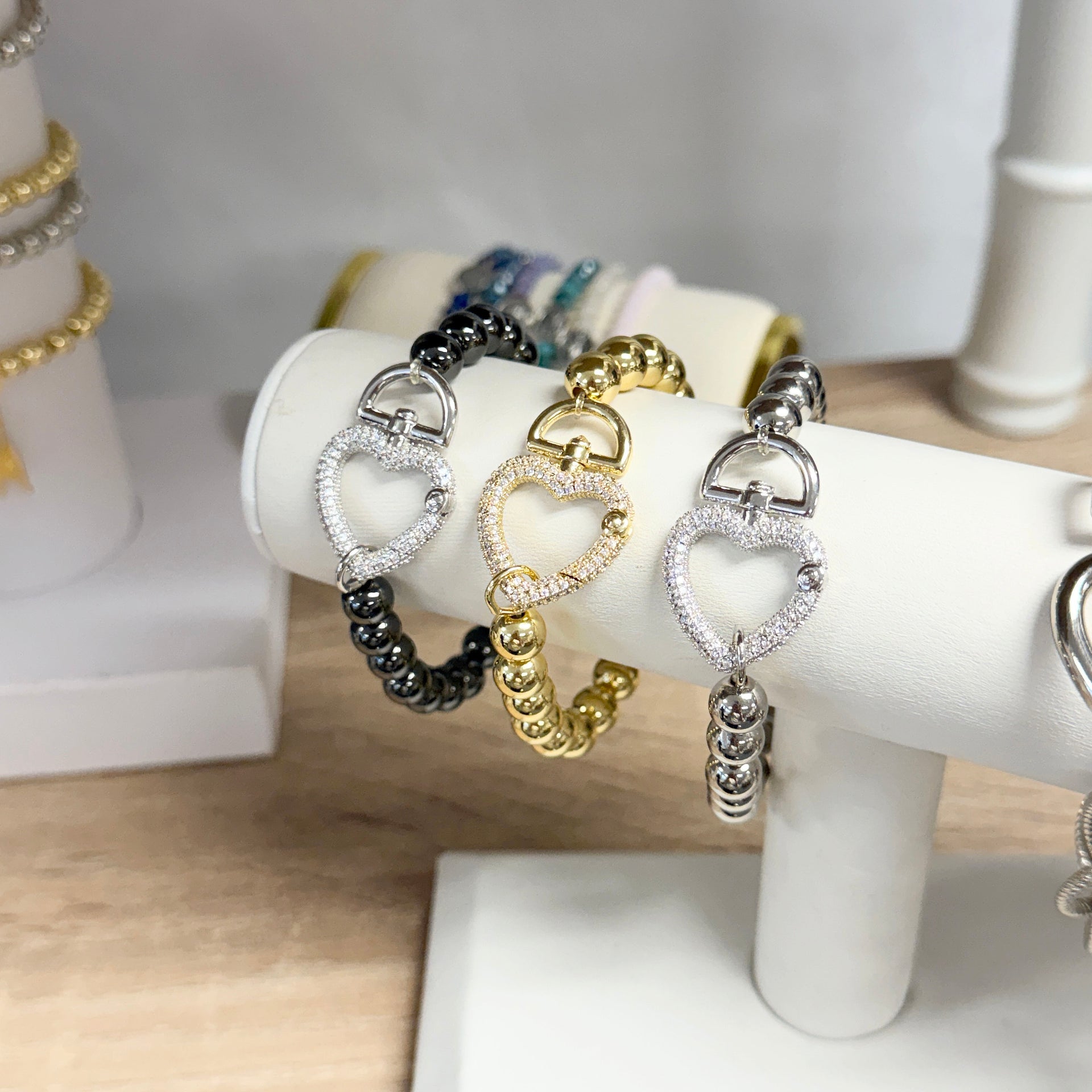 Heart-shaped bracelet with gold, silver, and black beads on a white stand.