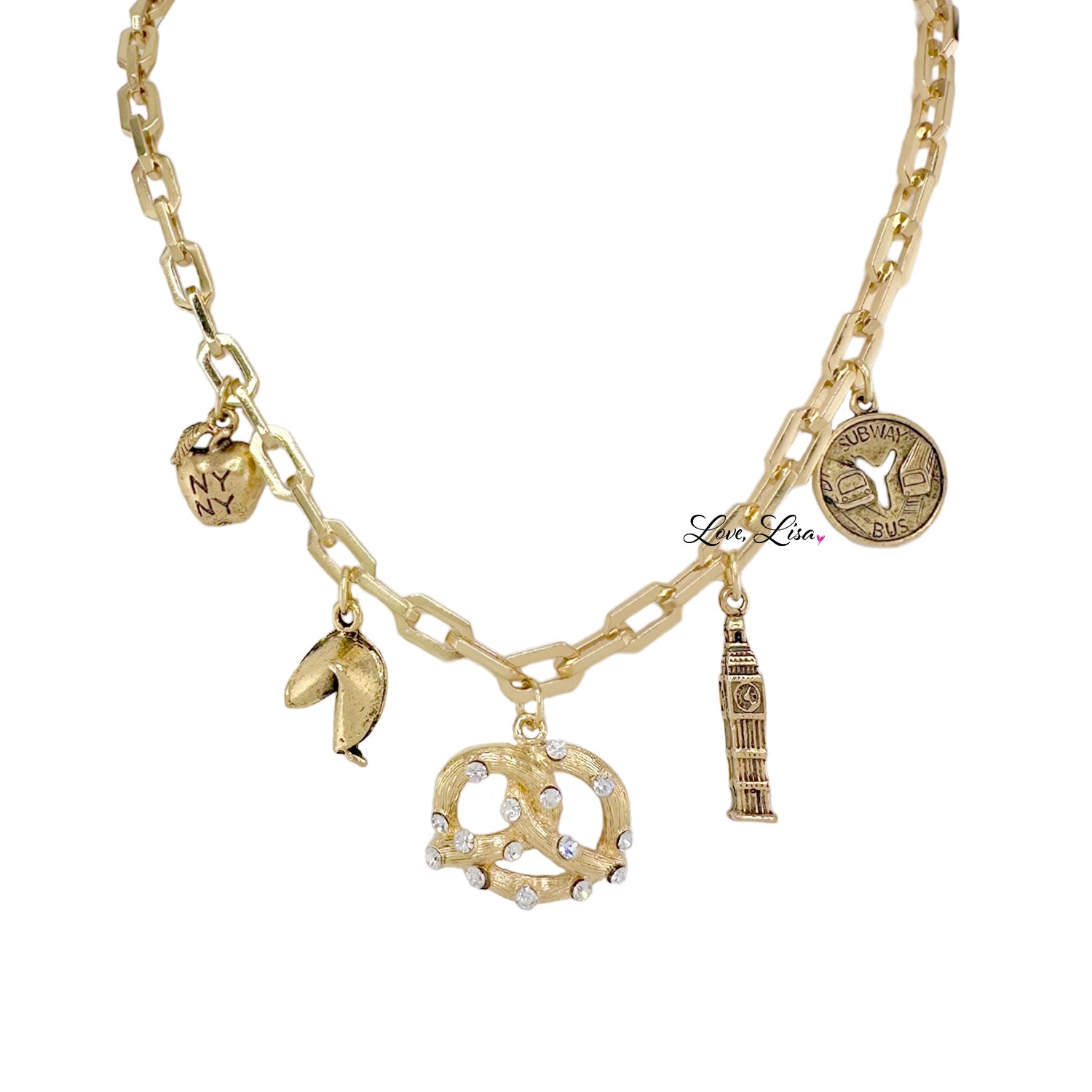 A gold-colored necklace with various charms including a pretzel, an apple, a subway token, and the 'I Love New York' emblem.