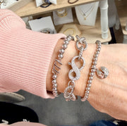 silver infinity clasp chain bracelet stacked on wrist with love lisa bracelets showing textured rope chain and crystal infinity clasp