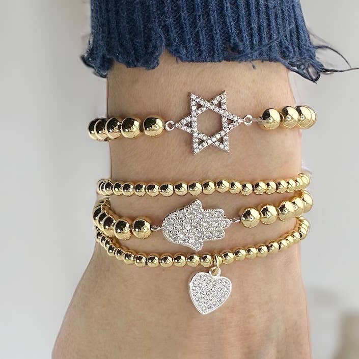 Gold bracelets with star, hand, and heart charms on a wrist against a neutral background