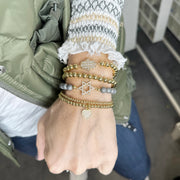 Hand wearing multiple bracelets with a green jacket and white shirt in the background