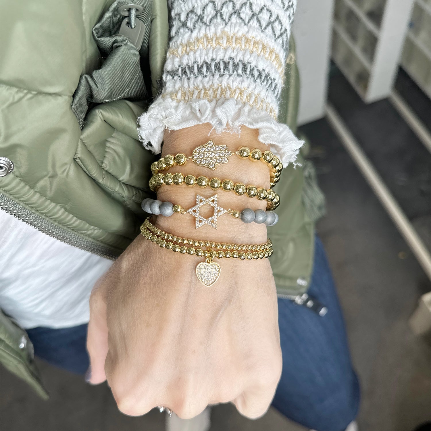 Hand wearing multiple bracelets with a green jacket and white shirt in the background