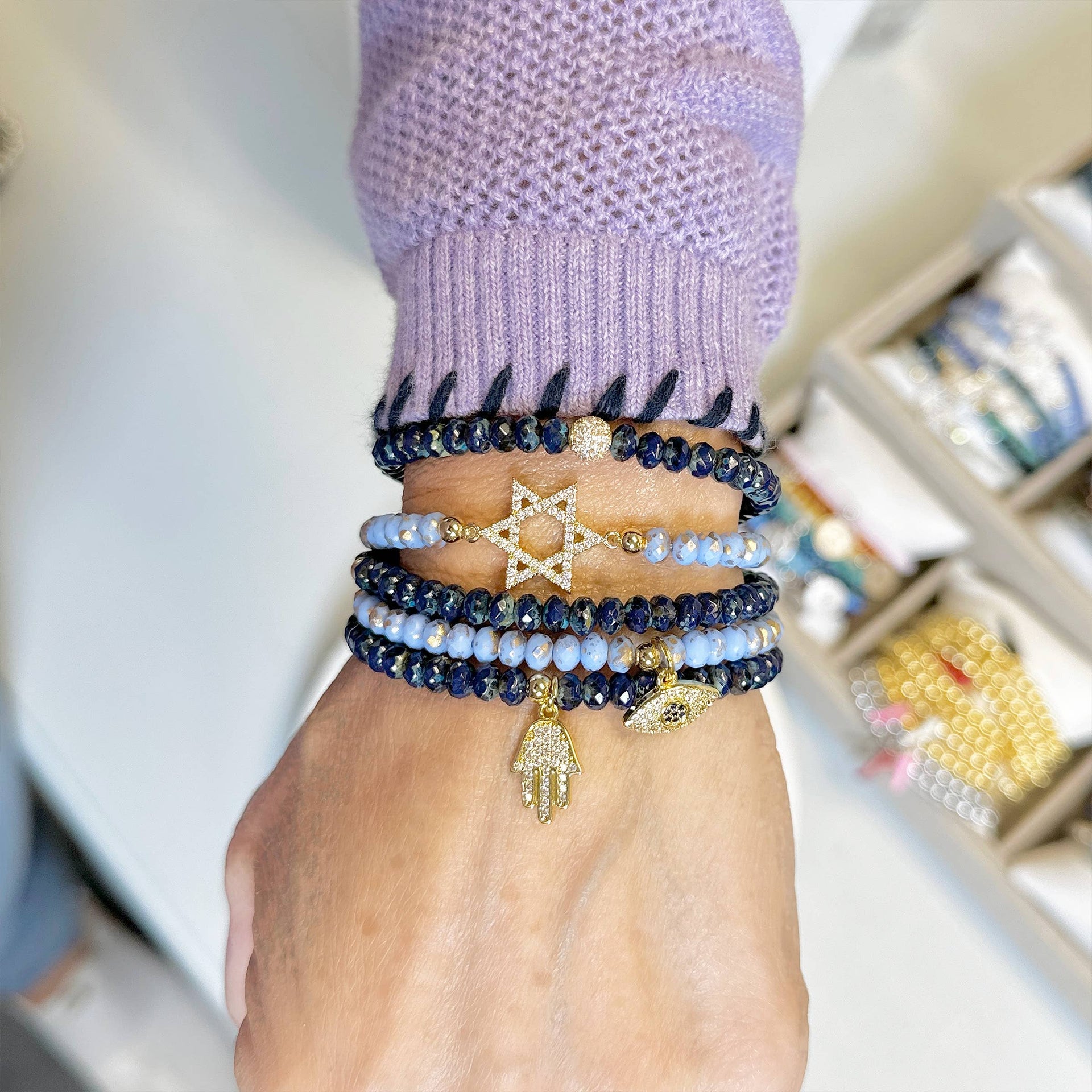 Hand wearing multiple beaded bracelets with star and hand charms on a blurred background