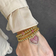 love lisa gold pink lila allure beaded heart bracelet shown stacked with multiple gold bead bracelets highlighting the pink pave heart charm for a layered wrist look