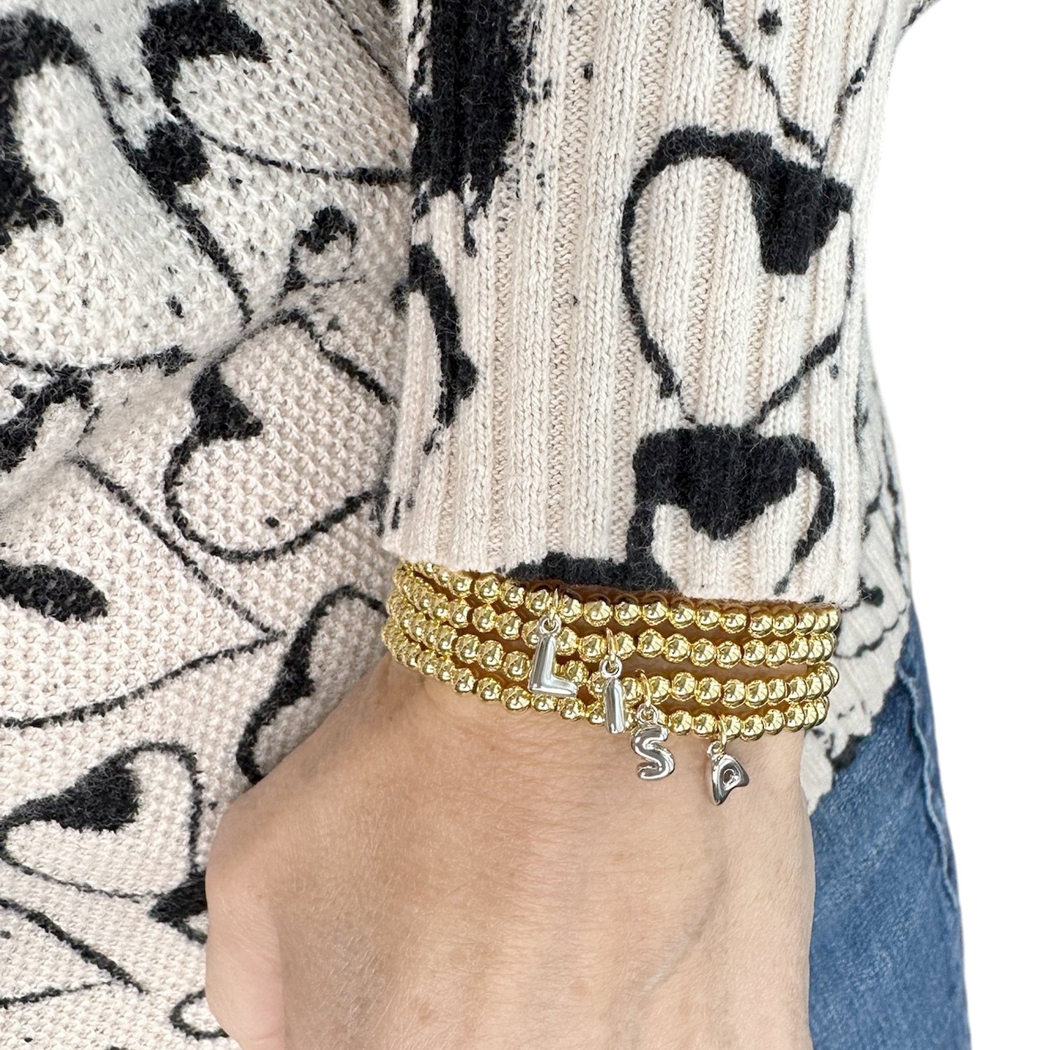 wrist wearing gold lila bubble letter initial bracelet styled with a cozy sweater for everyday look