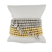 stack of gold and silver bubble letter initial bracelets displayed on jewelry pillow showing mix of initials