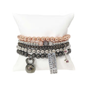 stack of workout inspired bracelets with mixed silver gunmetal and rose gold beads featuring dumbbell kettlebell helmet and Strong Is Beautiful tag on white pillow display
