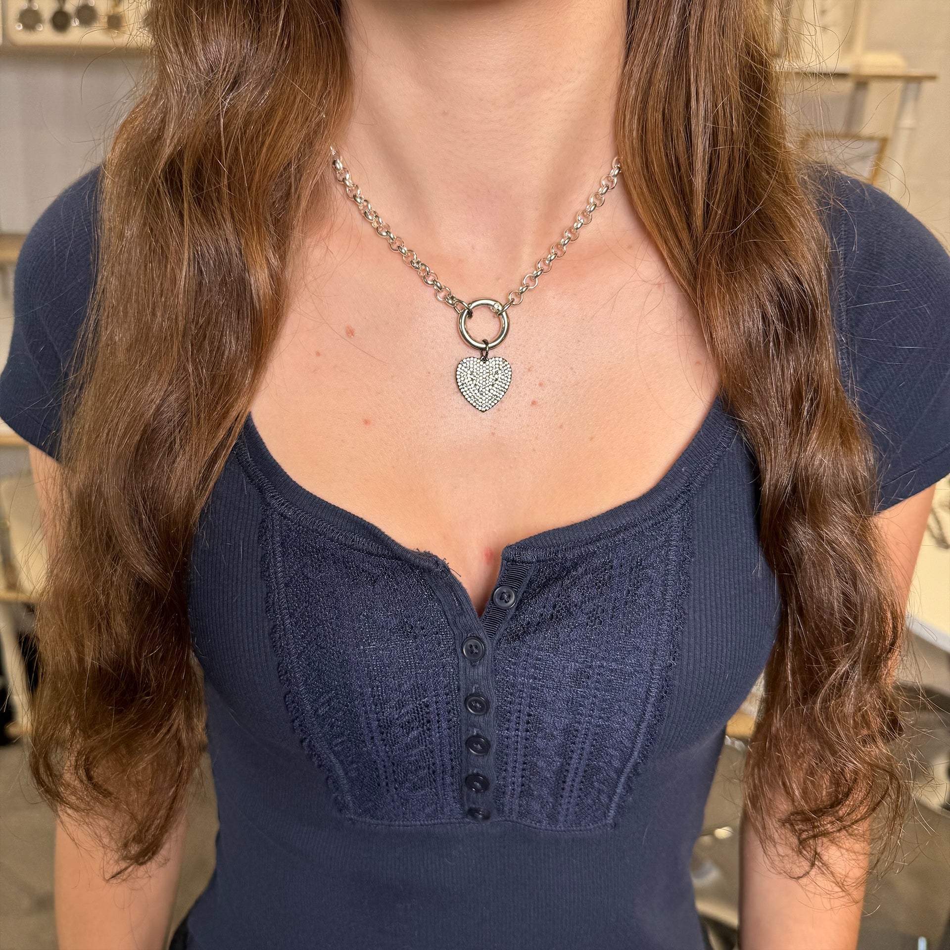 Person wearing a dark blue top and a necklace with a heart pendant.